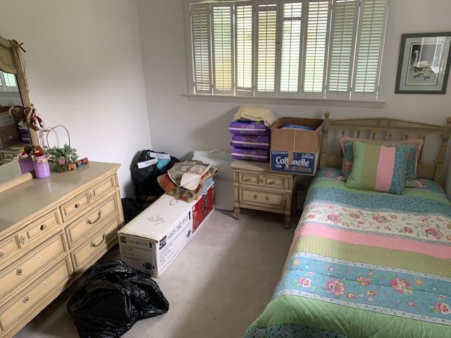 Bedroom with a bed, dresser, window, and storage boxes cluttering the floor and corner.