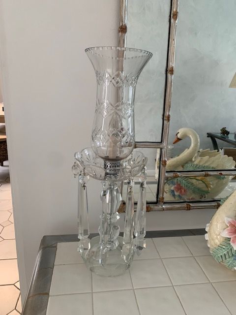 Tall clear glass vase with dangling crystal prisms on a tiled floor by a mirror and ceramic swan decor