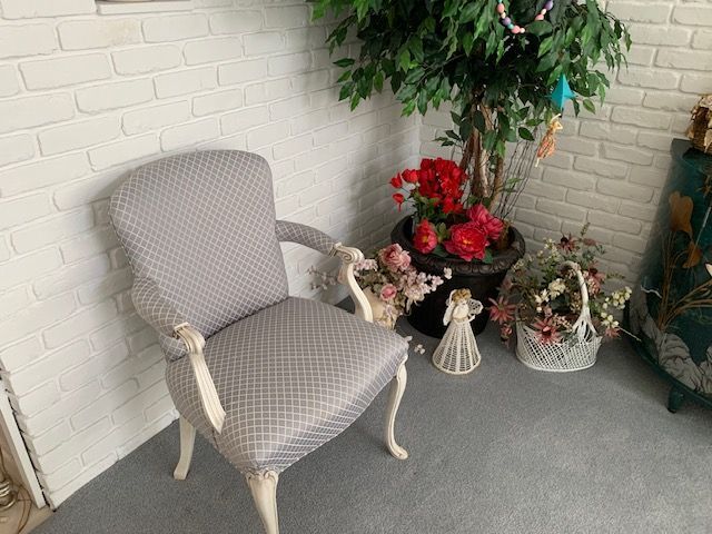 Gray upholstered chair in a corner with white brick walls, beside potted red flowers and a small decorative lantern