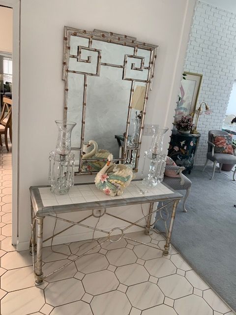 Decorative console table with mirror, glass vases, and floral vase in a tiled entryway
