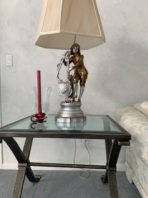 Glass side table with a lamp, red candle, and small horse figurine next to a couch
