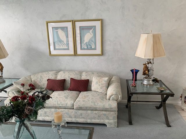 Living room with a cream sofa, red pillows, glass side table, lamps, and framed wall art.