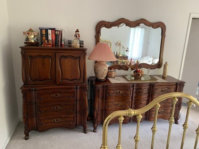 Vintage bedroom with carved wooden dresser, vanity mirror, lamp, and brass bed frame