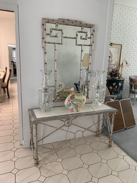 Decorative console table with ornate mirror, glass vases, and plates in a bright tiled room
