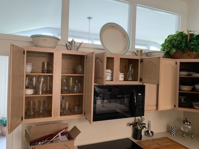 Light wood kitchen cabinets with glass doors, microwave, dishes, and plants on the counter