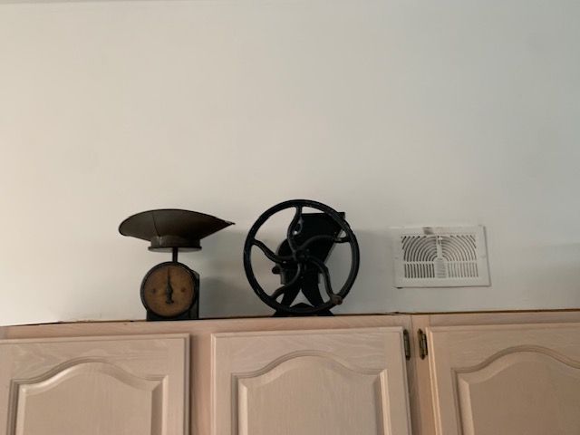 Decorative shelf with a black nautical wheel and a small lamp above beige cabinets