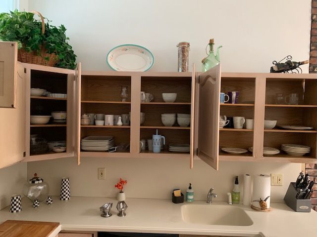 Kitchen with open wooden cabinets, dishes, mugs, and decor above a countertop and sink.