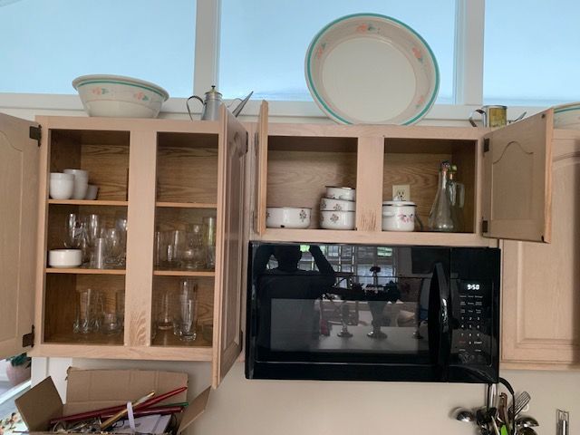 Kitchen cabinets and countertop with a microwave, dishes, and open wooden cabinet doors.