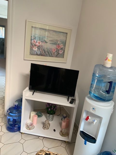 Small corner with a TV on a white stand, wall art, and stacked water coolers on the right.
