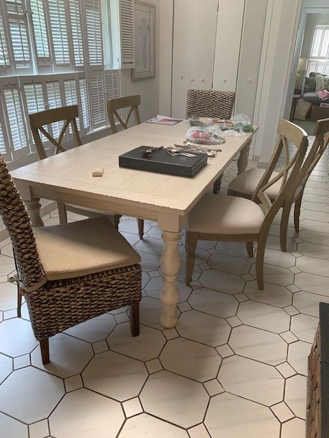 Dining room with white table, mixed chairs, and a tray on the tabletop, lit by natural light.