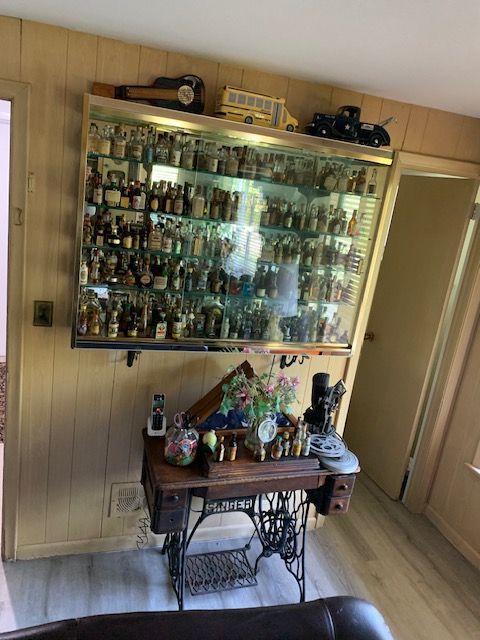 Glass display cabinet filled with collectibles above a small ornate table in a wood-paneled room