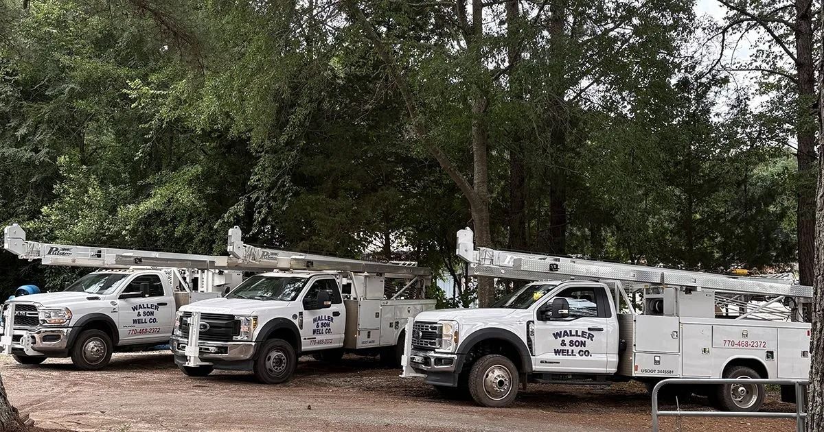 Three white utility trucks with boom lifts parked in a row in a wooded area.