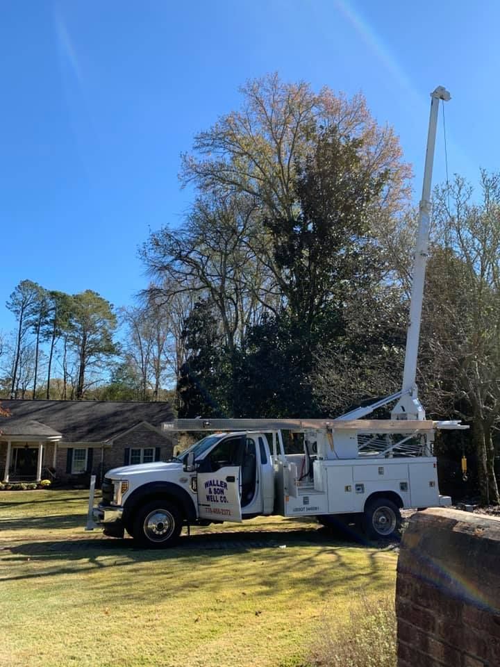 A white utility truck with an extended crane arm parked on a residential lawn under a clear blue sky.