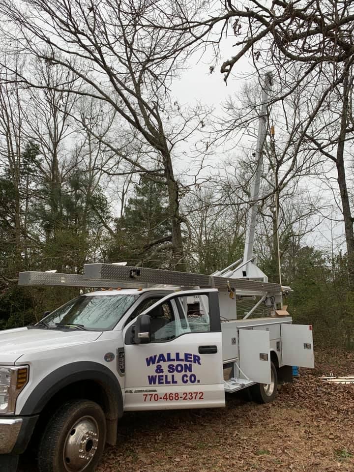 White truck with a tall drill rig, parked near trees; 