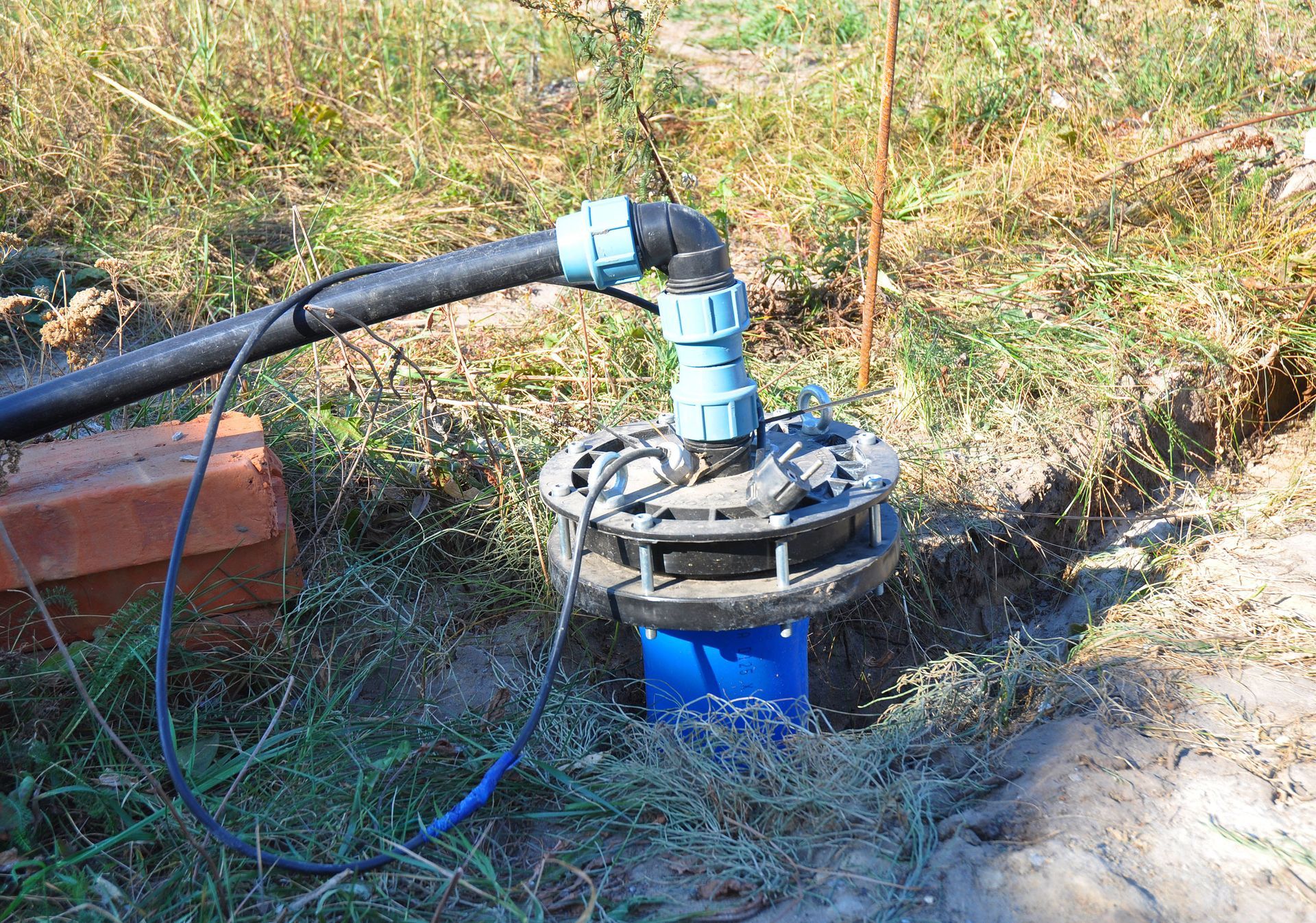 Well pump with black pipe and blue fittings, installed in the ground.