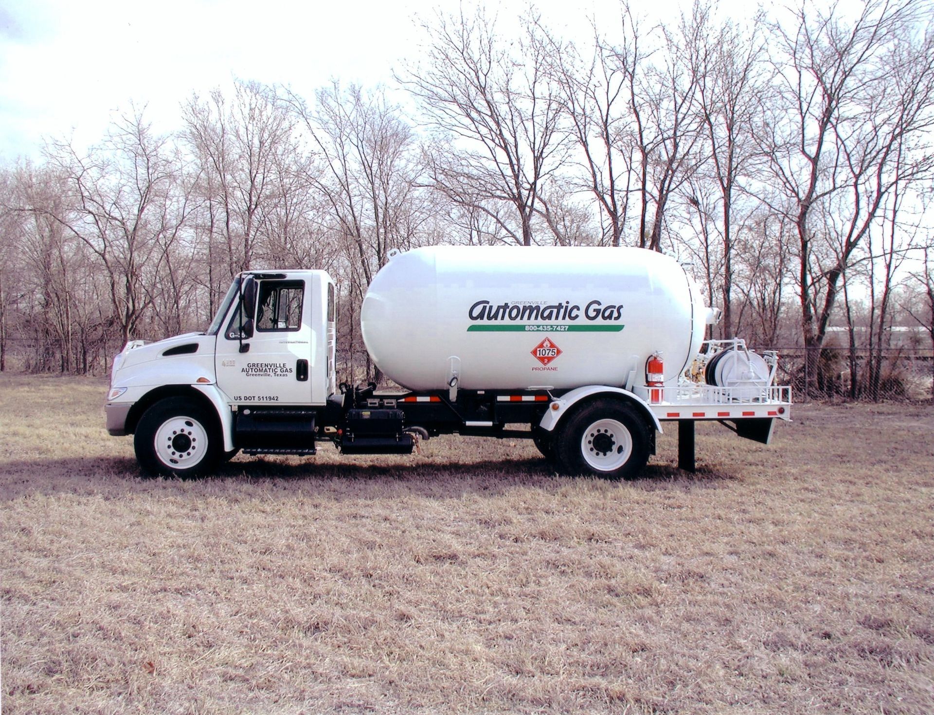 White propane delivery truck parked in a field with trees in the background. 