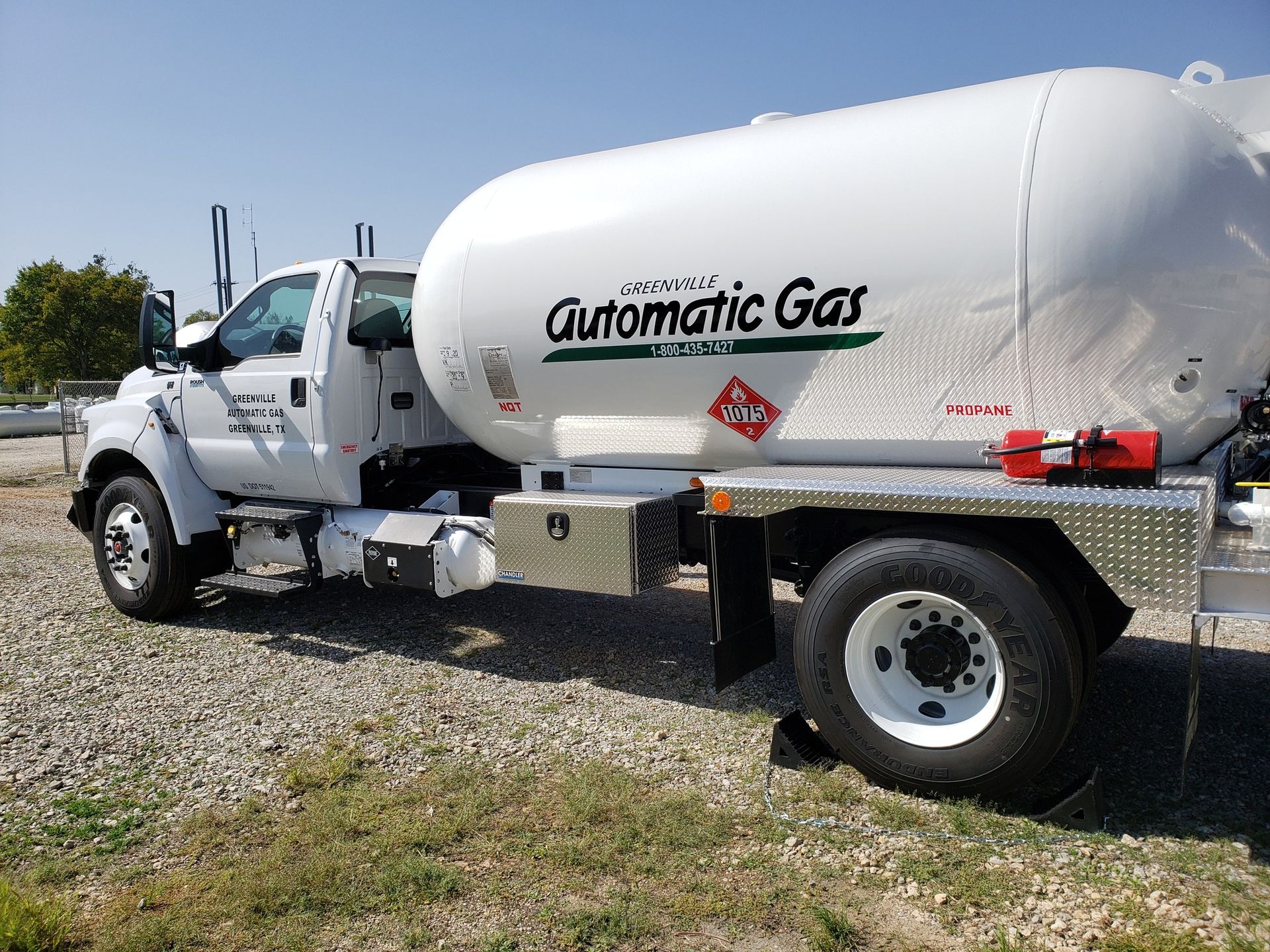 White Automatic Gas truck with a large tank, parked on a grassy area, clear sky.