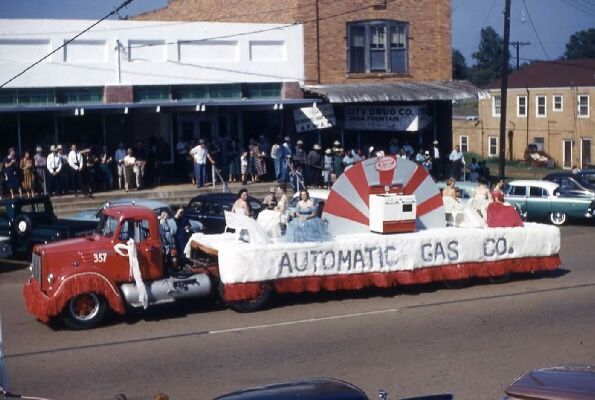 Parade float for Automatic Gas Co., with red truck, people, and buildings in the background.