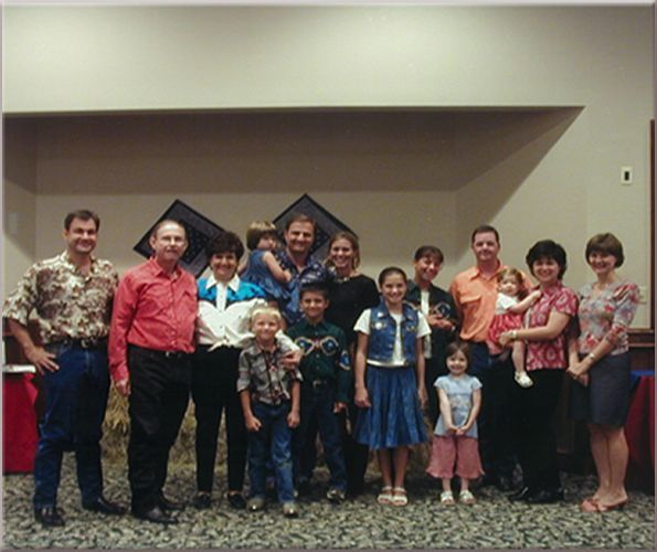 Group of people posing indoors in front of decorative wall art. Some are holding children, smiles.