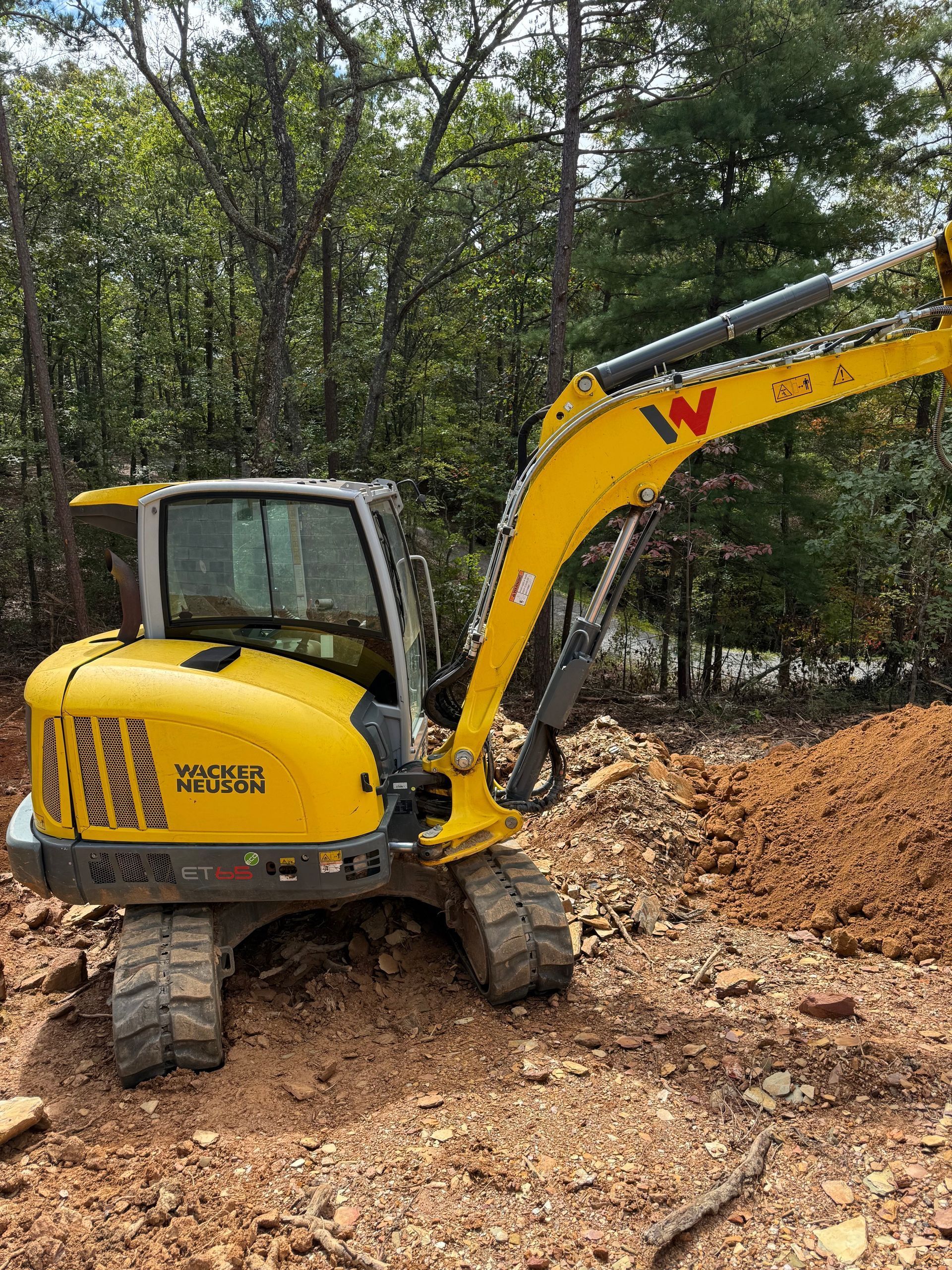 Yellow excavator digs in a dirt area with trees in the background.
