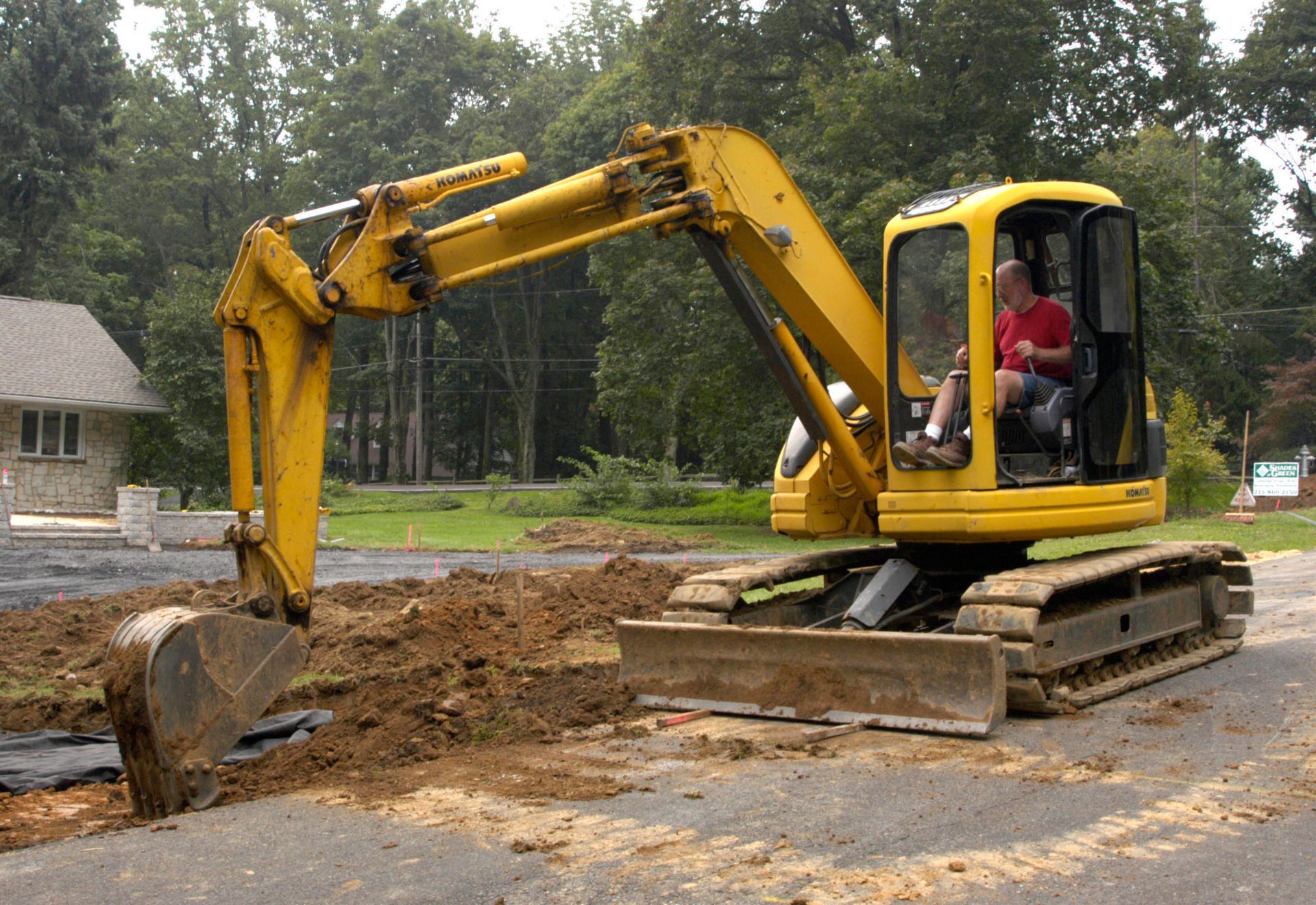Yellow excavator digging earth on a road; a person is in the cab.