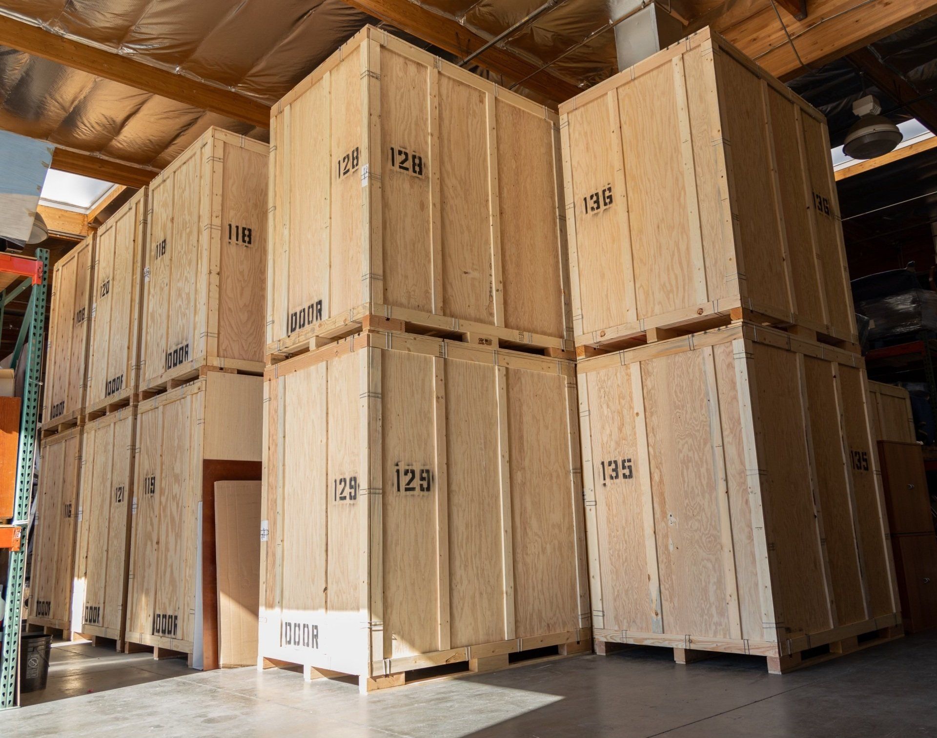 Wooden crates stacked in a warehouse, numbered 123, 125, and 128, sit on pallets.