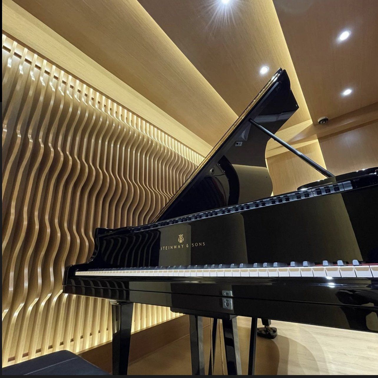 Black grand piano in a music studio with wood-paneled wall.