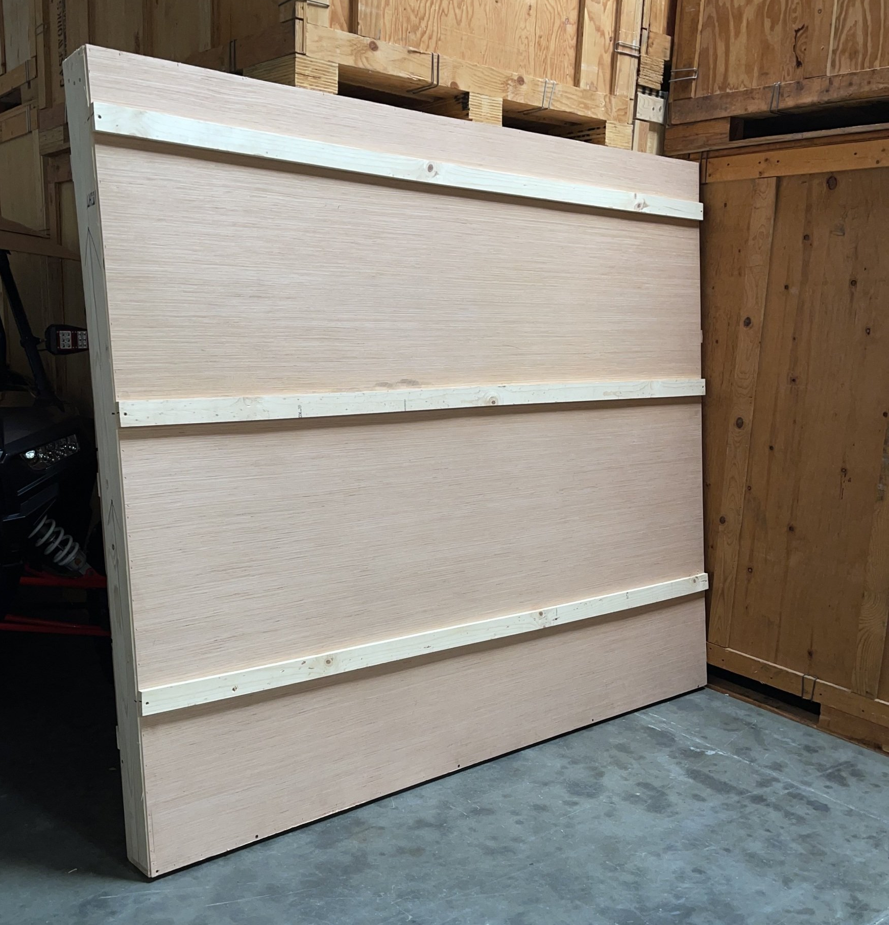 Large wooden panel with three horizontal wooden supports, propped against wooden structures.