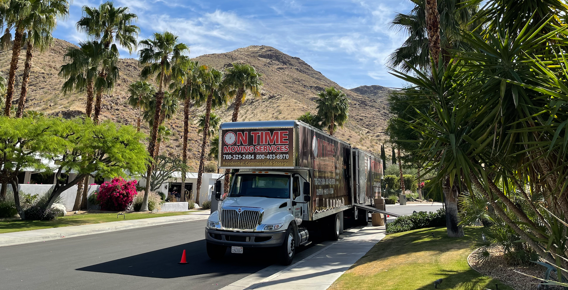 Truck parked on street in front of a house, palm trees, and mountains. Truck has the name 