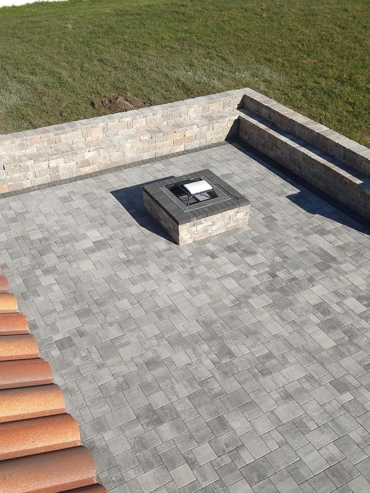 Patio with gray pavers, stone fire pit, and a wall with built-in seating; grass in the background.