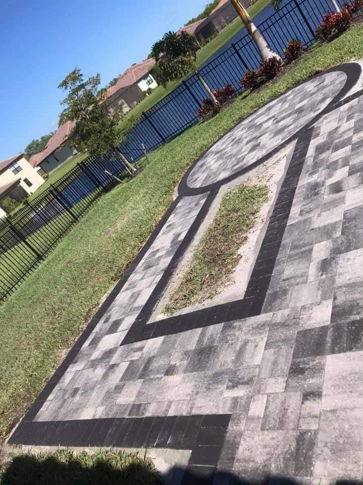 Brick patio with black borders and circular features, overlooking a fence and water, sunny day.