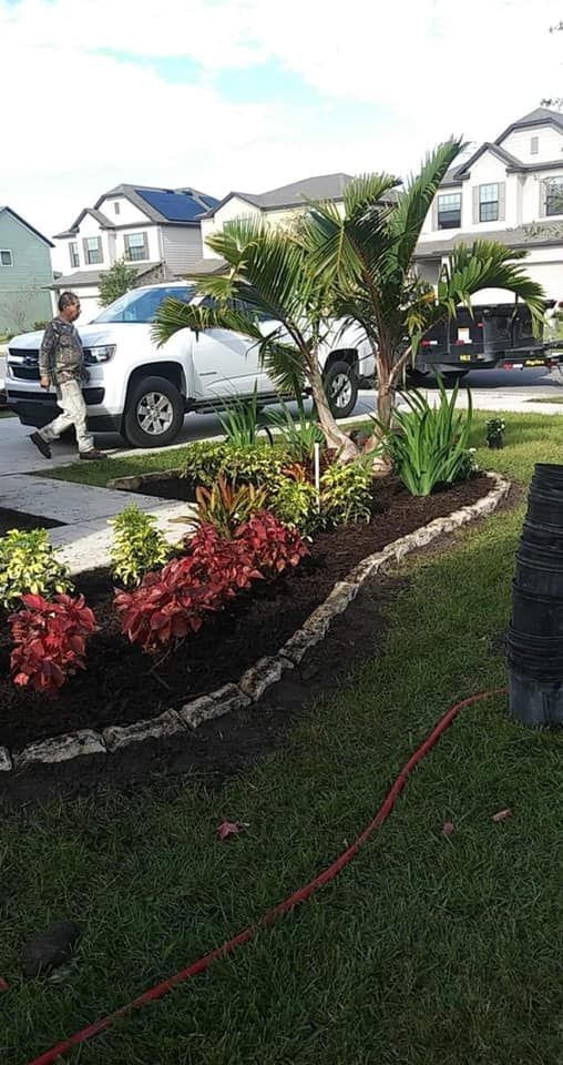 Landscaped yard with colorful plants, a palm tree, and a man walking near a white truck.