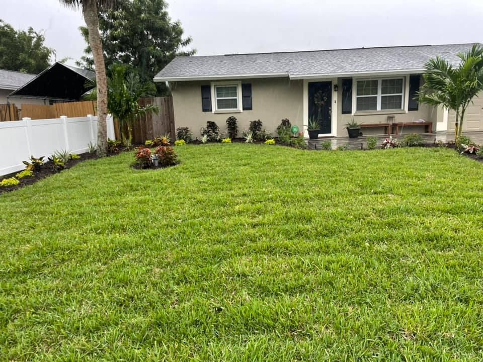 A well-manicured green lawn leads to a tan house with dark trim and a dark gray roof.