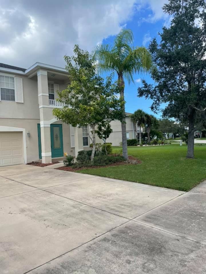 Two-story house with tan stucco, green door, and palm tree in front yard, driveway and sidewalk.