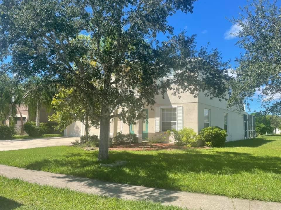 Two-story house with green lawn, trees, and blue sky.