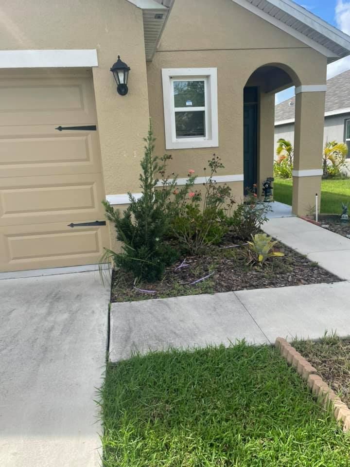 Beige house with a small garden bed next to the front door, next to a garage door.