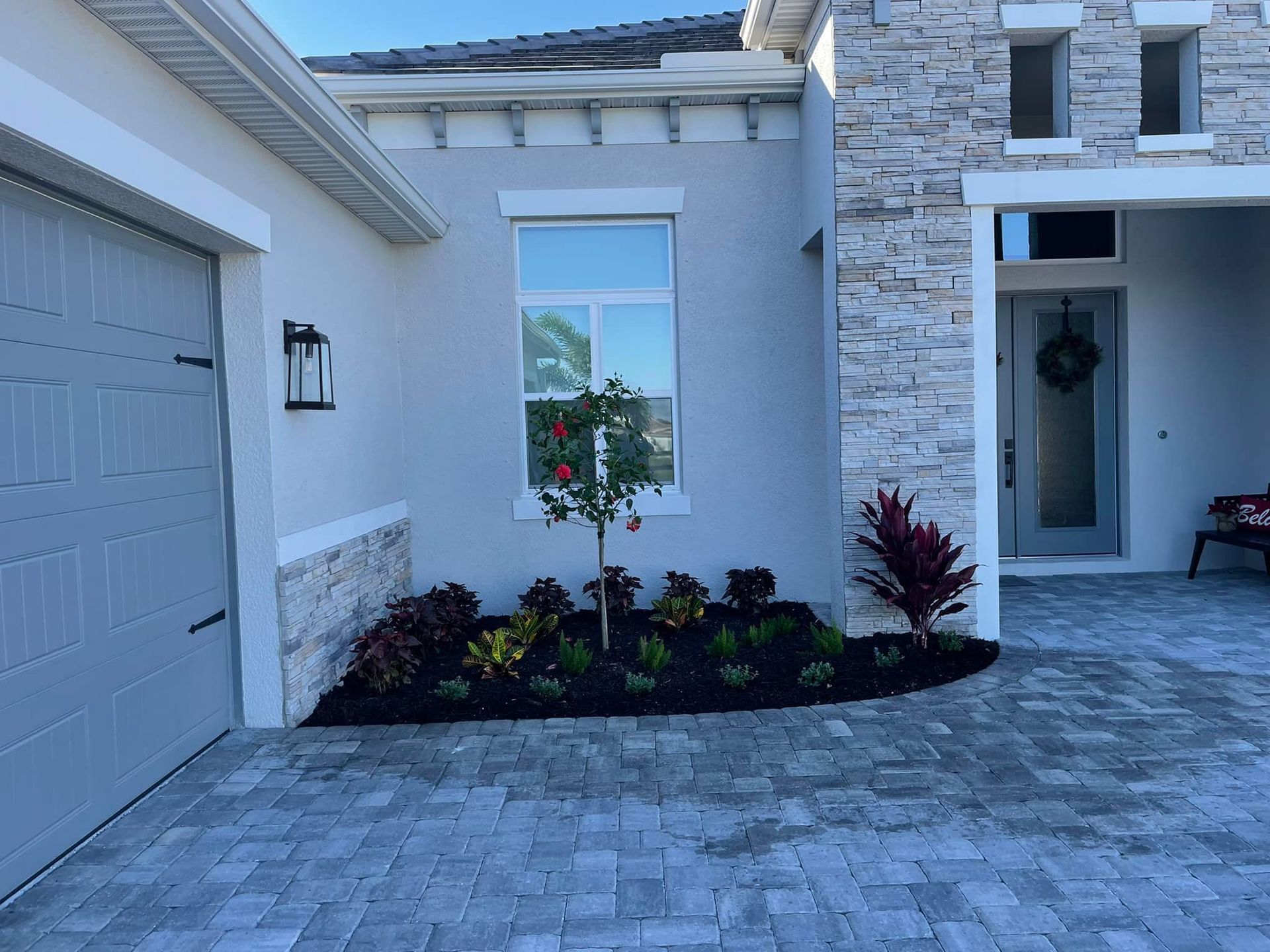 Exterior of a modern house with a landscaped garden bed and a gray paved driveway.