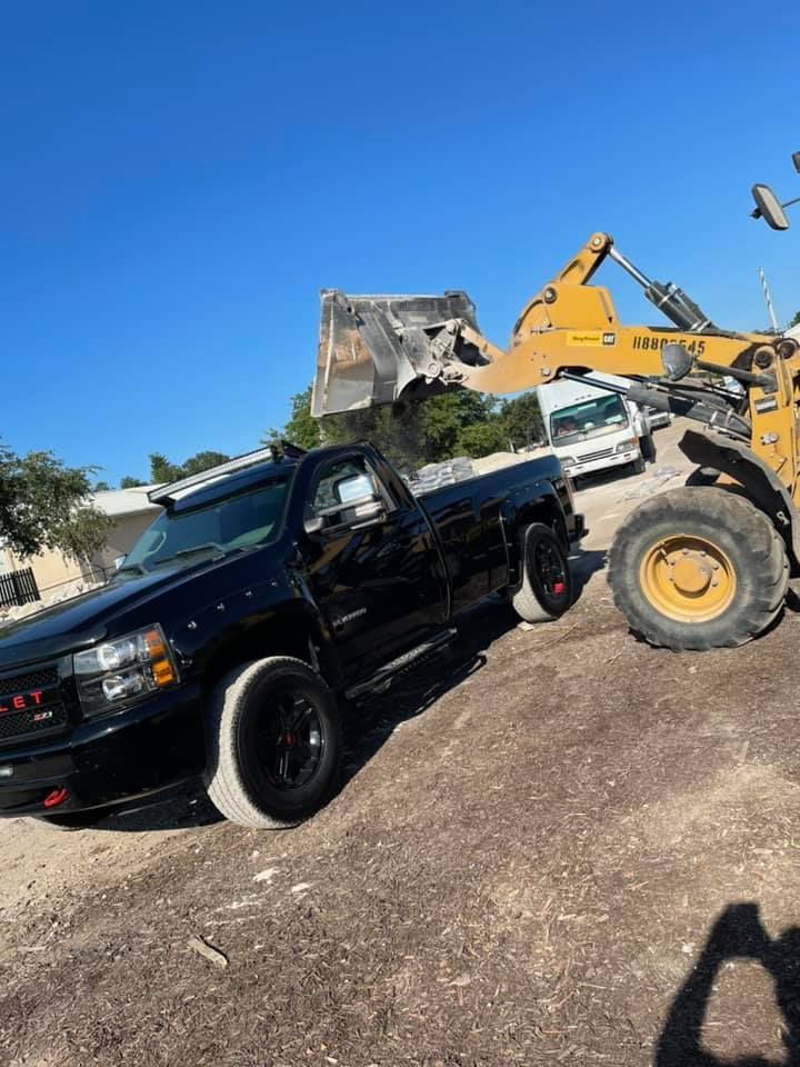 Black pickup truck on dirt slope, yellow bulldozer in background. Sunny day.
