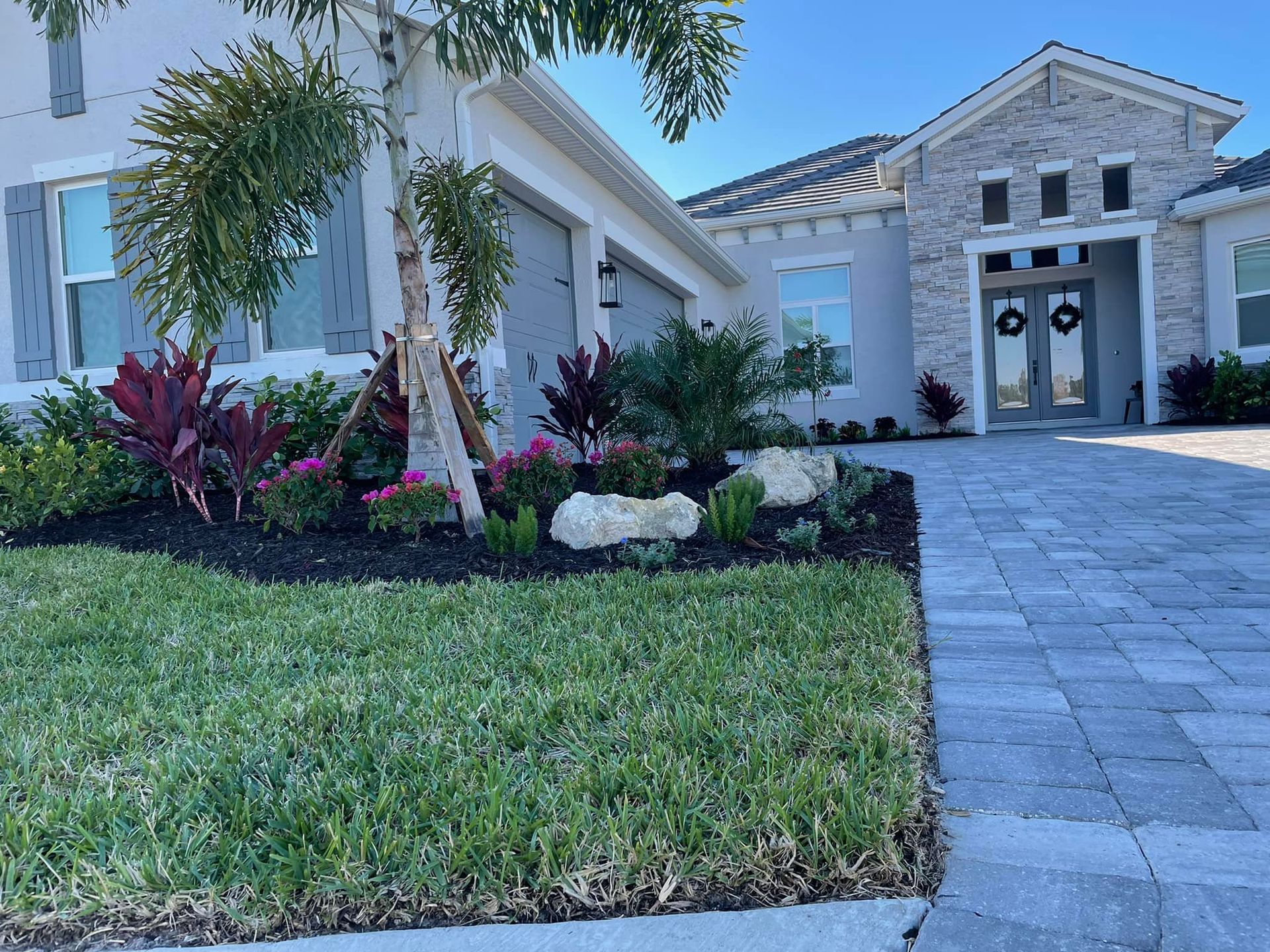 Well-maintained house exterior with landscaping, green grass, and a paved driveway.