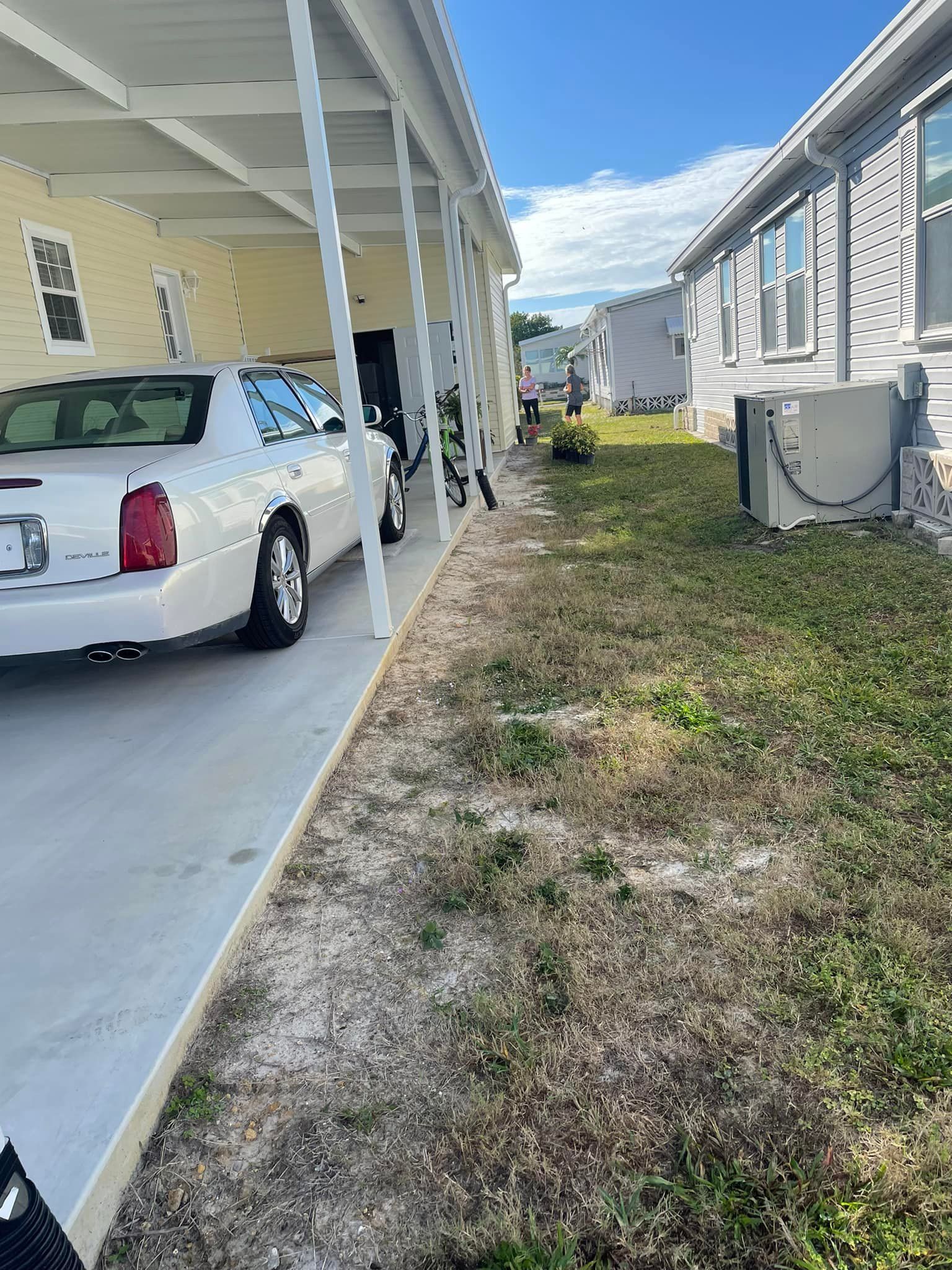 White car parked next to a carport with a grass yard, sunny day.