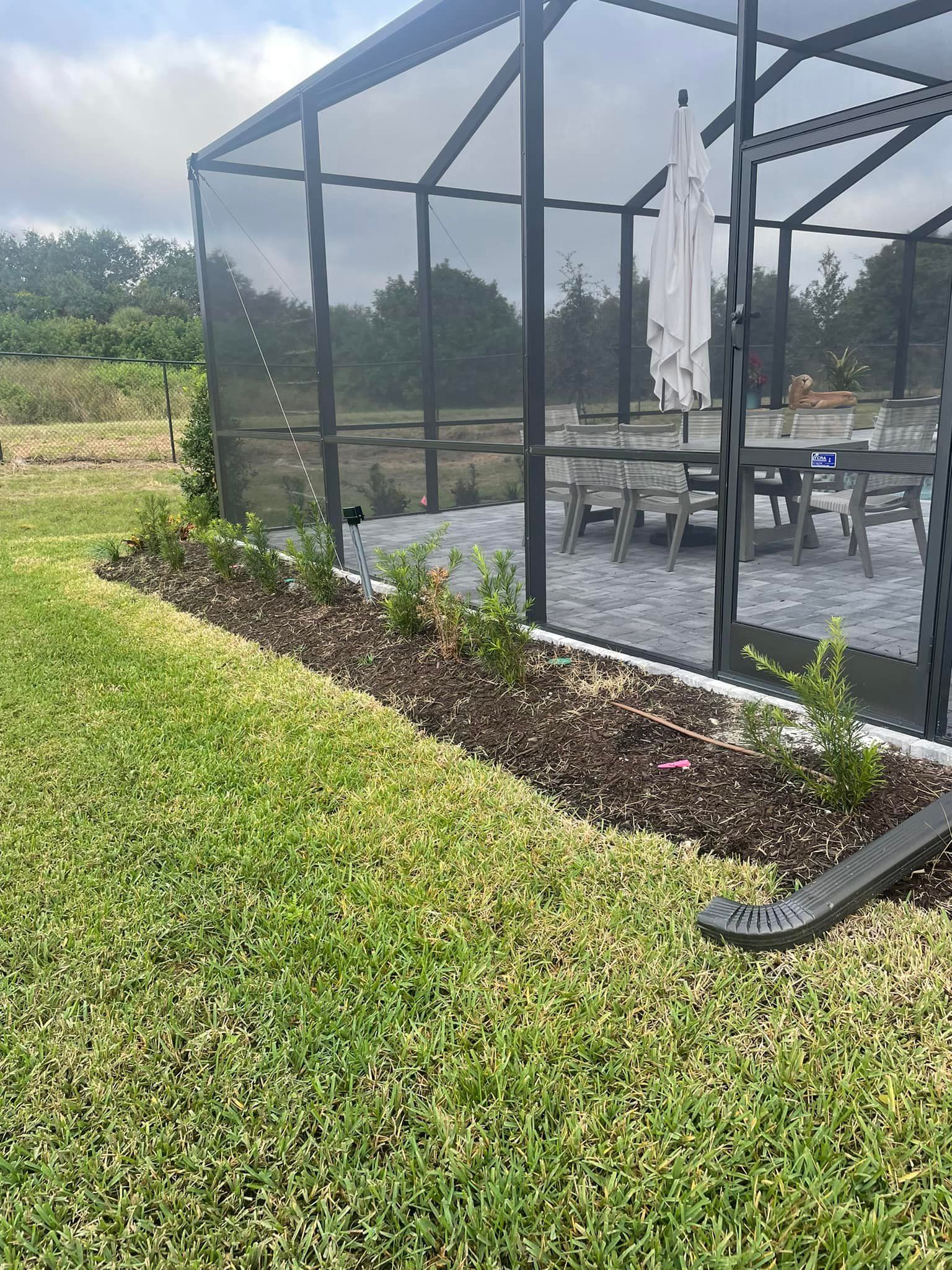 A screened-in patio with a dining set, surrounded by landscaping and lawn.