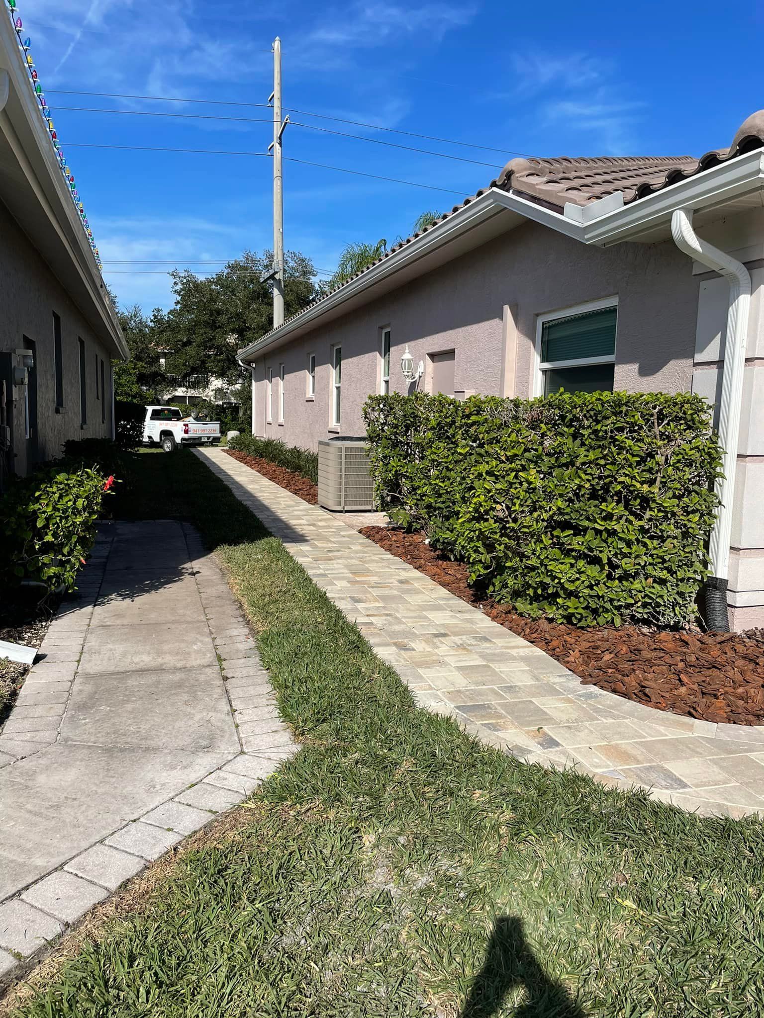 Pathway between two buildings, brick path, green lawn, blue sky, hedges, and utility pole.