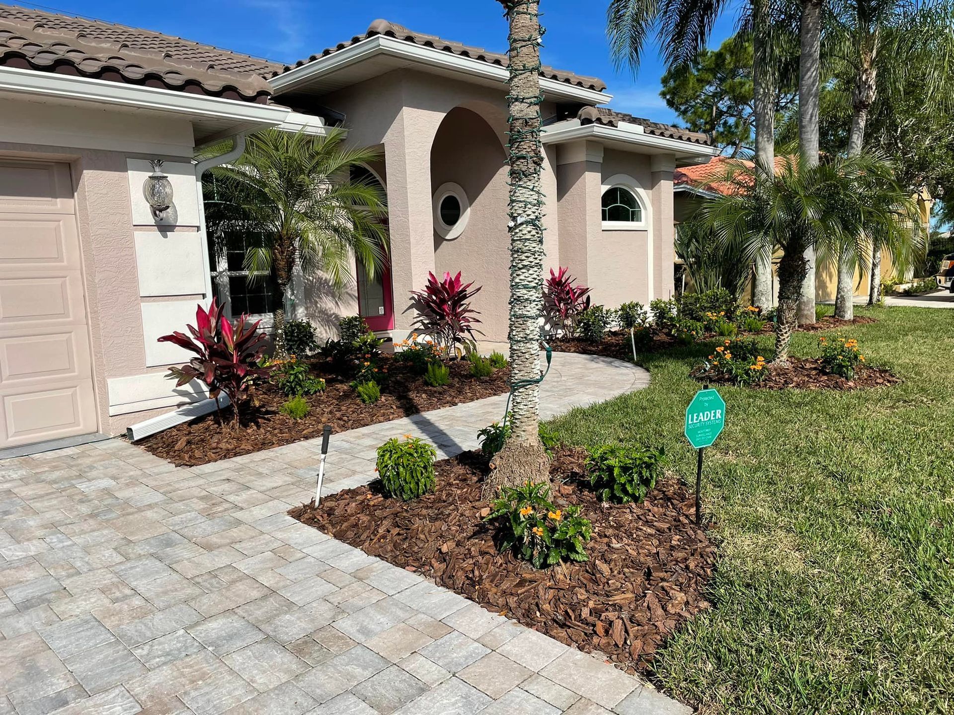 A beige house with a brick walkway and well-manicured landscaping, including plants and mulch.