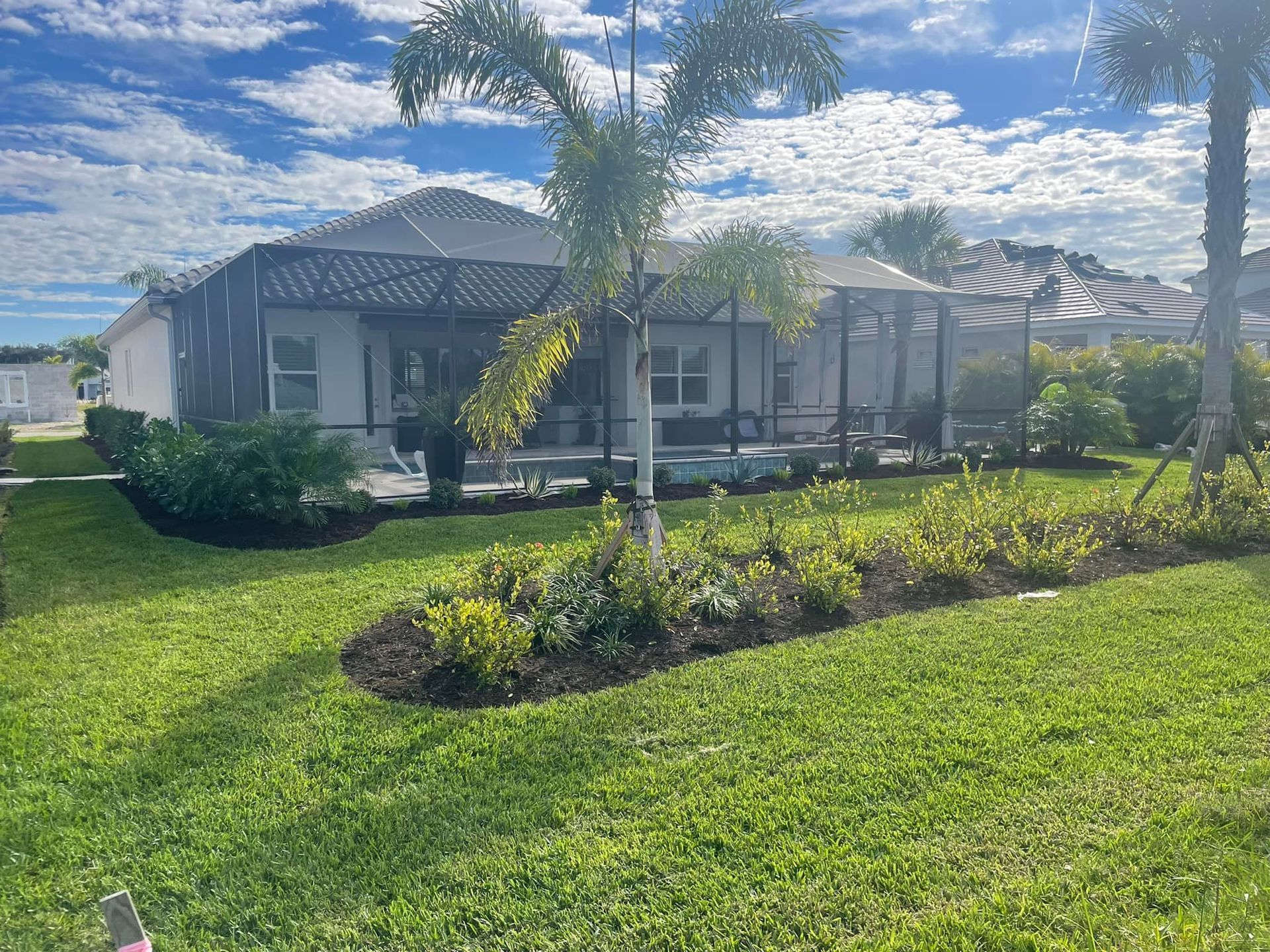 House with screened patio, palm tree, and landscaped yard under a cloudy sky.