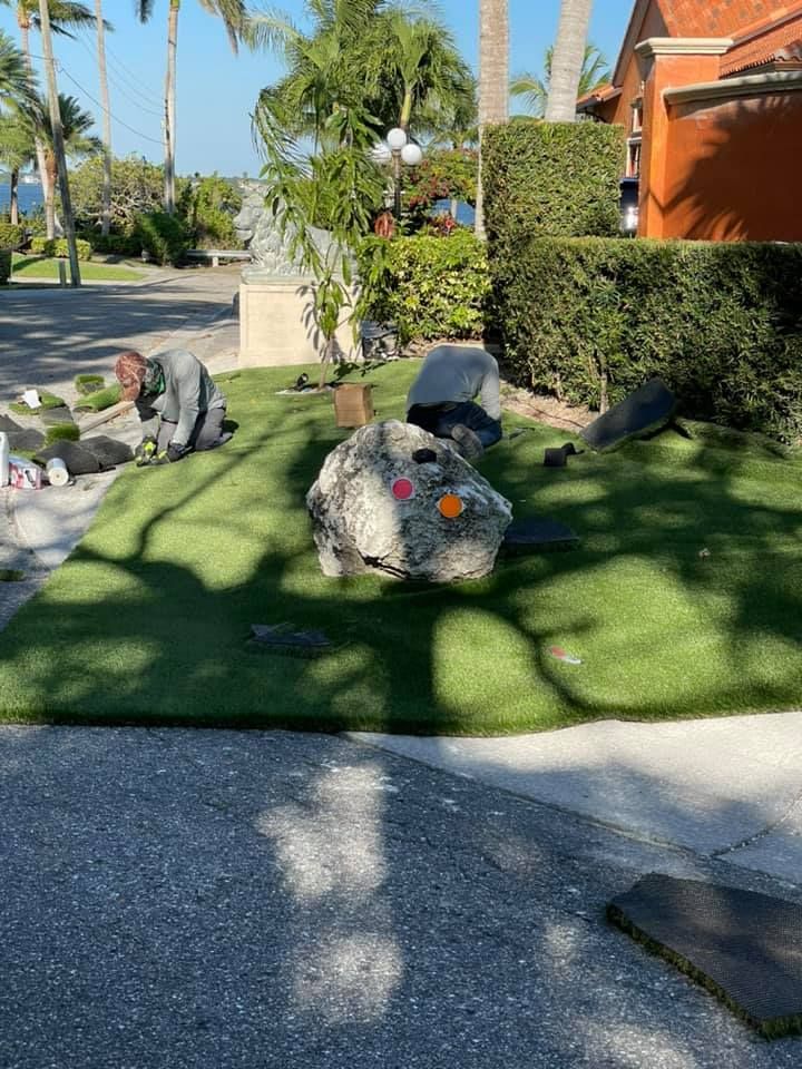 A person working on landscaping with rocks and artificial turf; sunny outdoors.