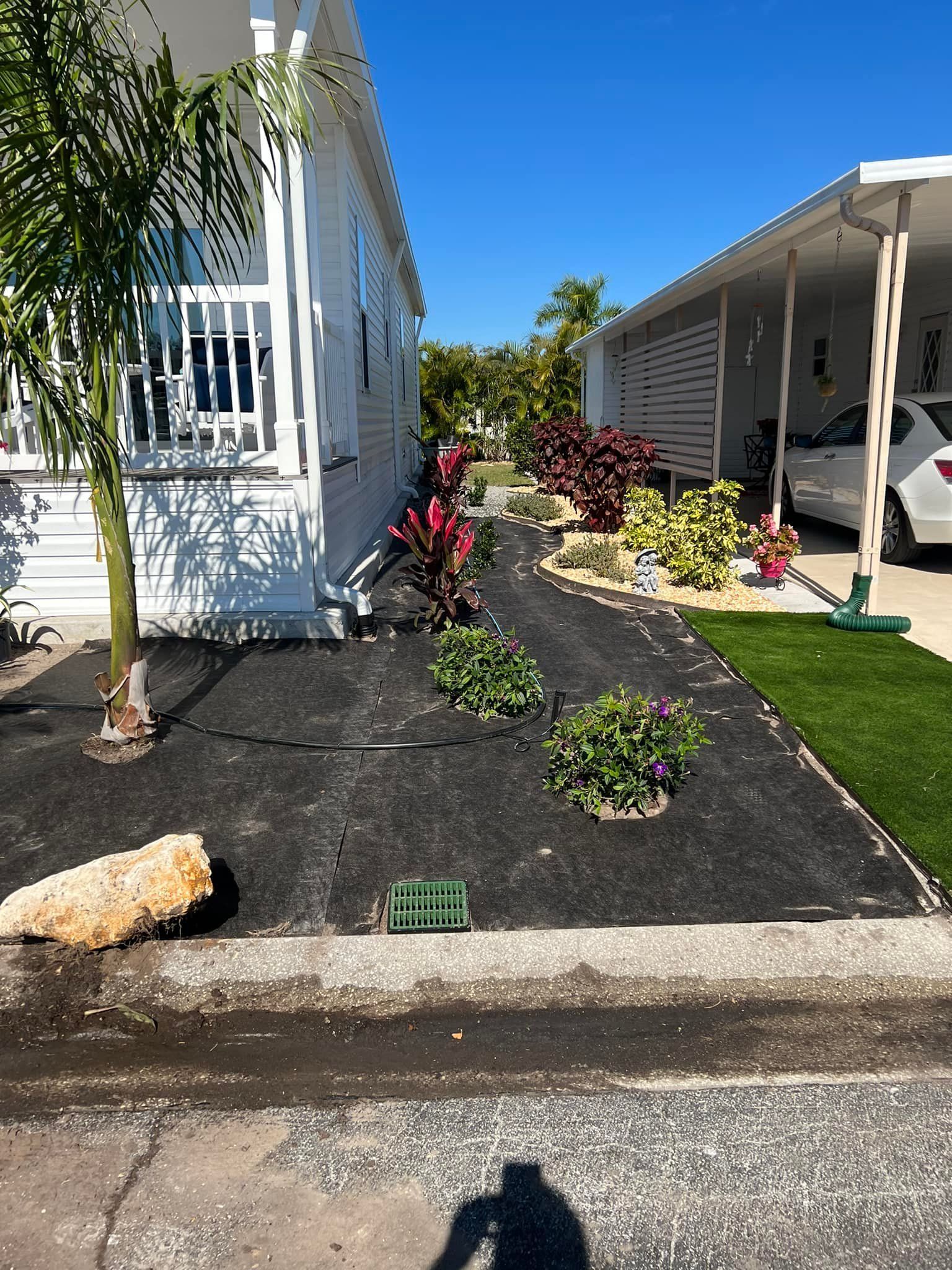 Landscaped front yards of two adjacent houses, one with a car, blue sky.