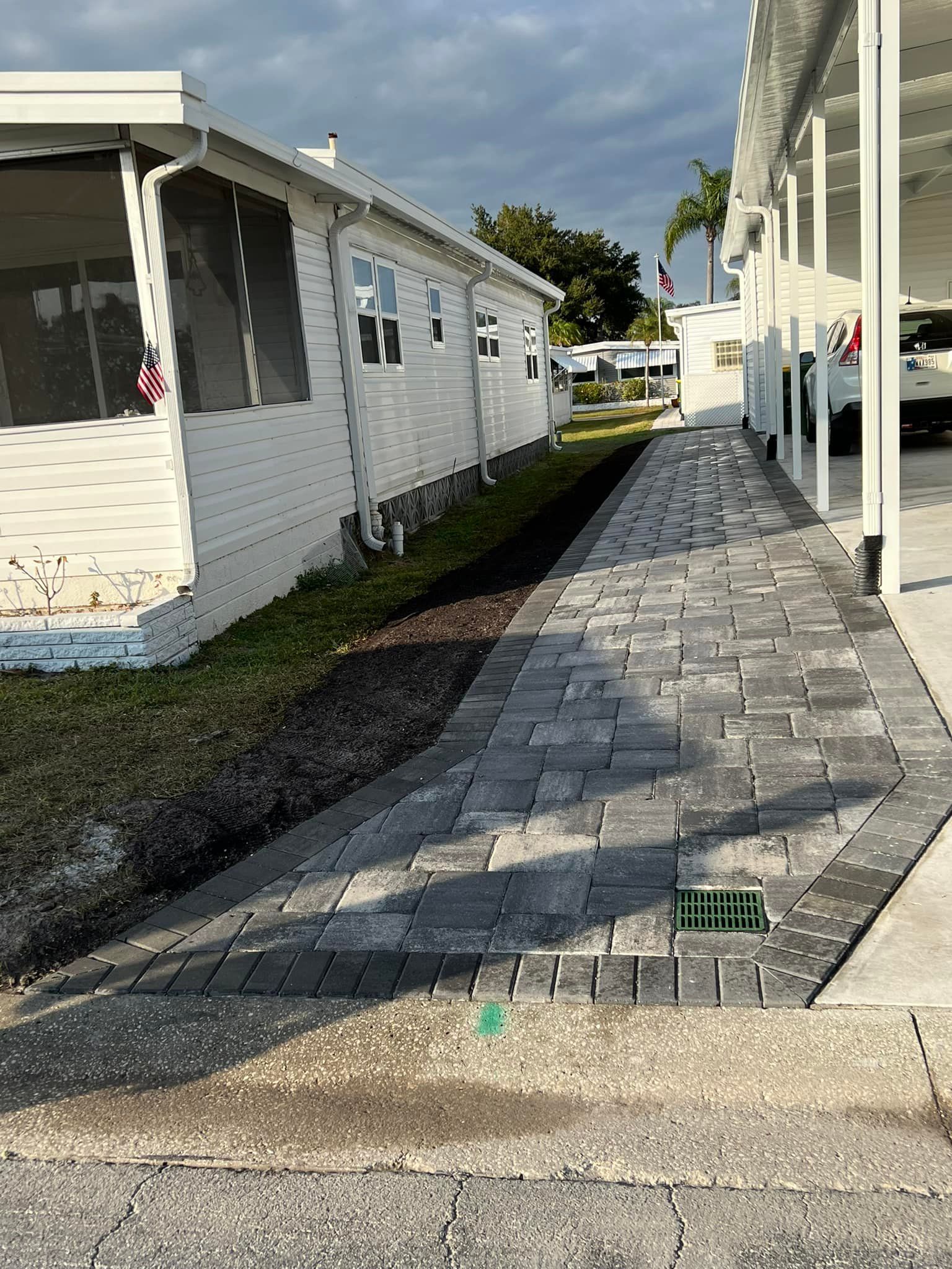 Stone walkway between white buildings, leading to a street. Dark mulch bed on the left.