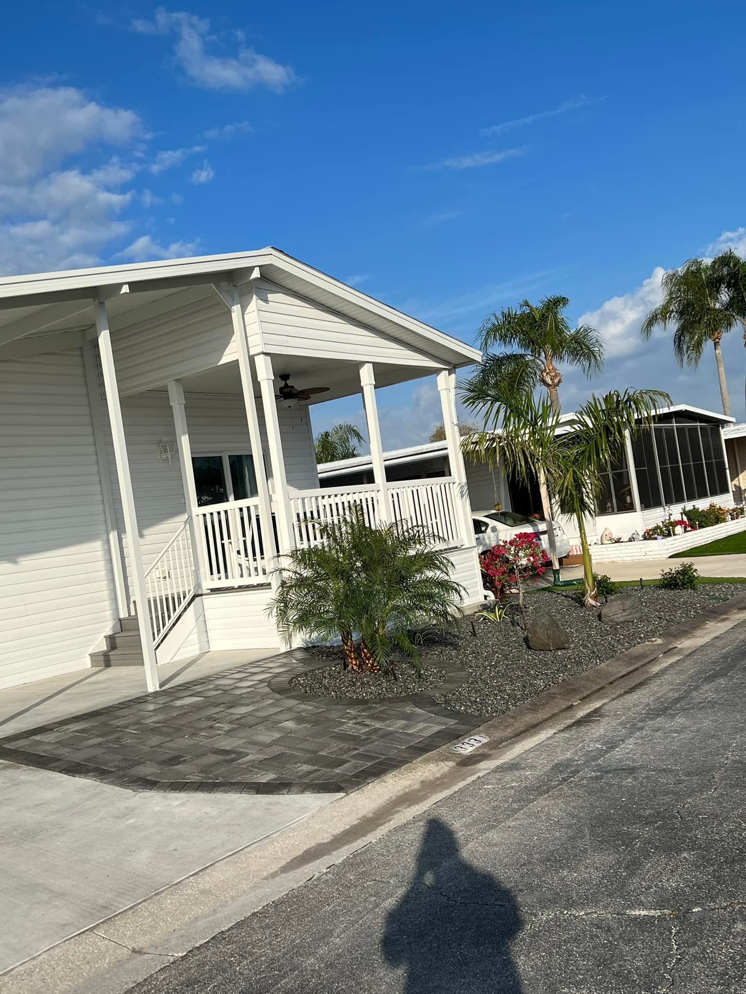 White house with a porch, palm trees, and blue sky.
