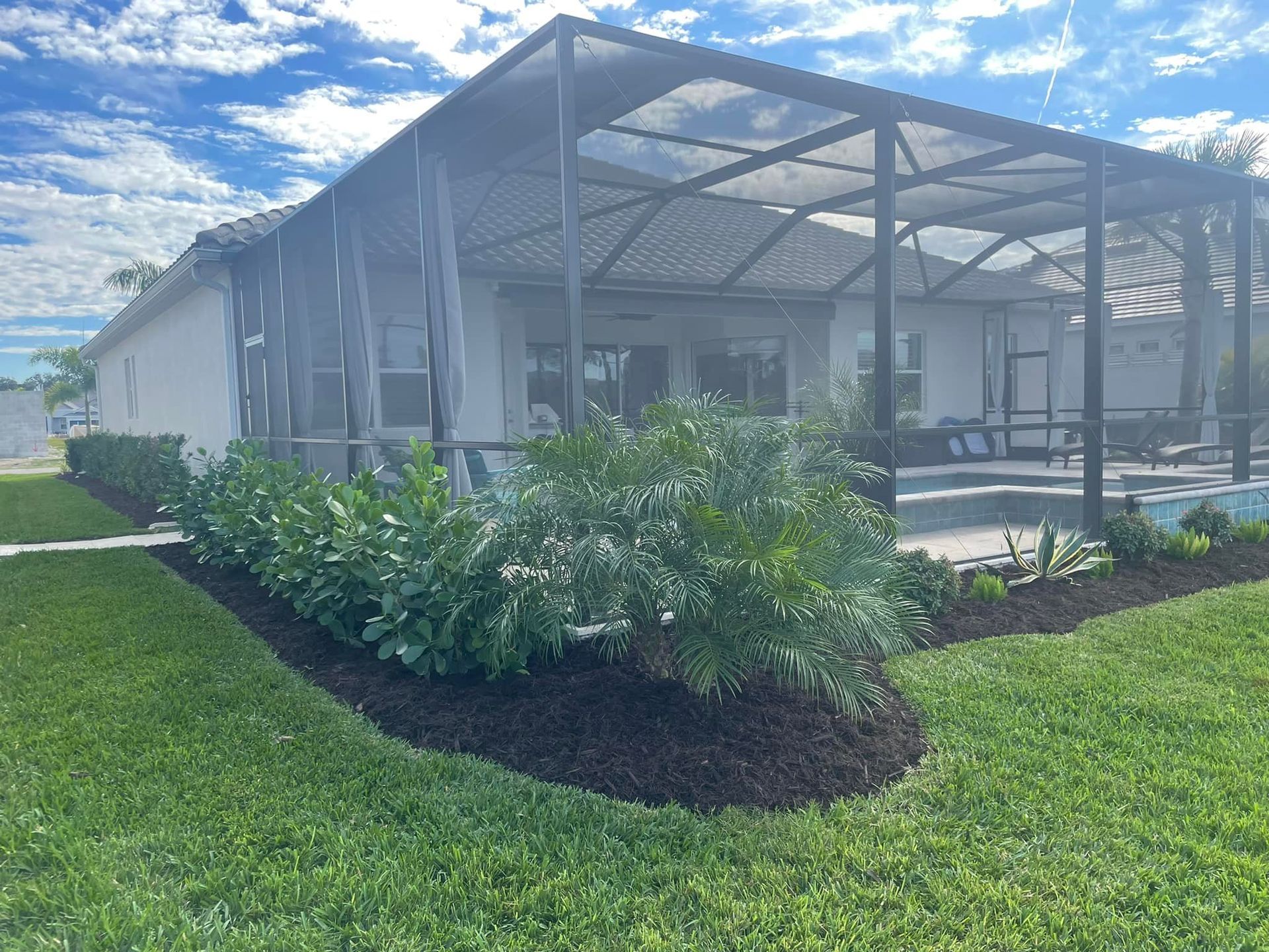 A house with a screened-in patio, pool, and green lawn, with blue sky.