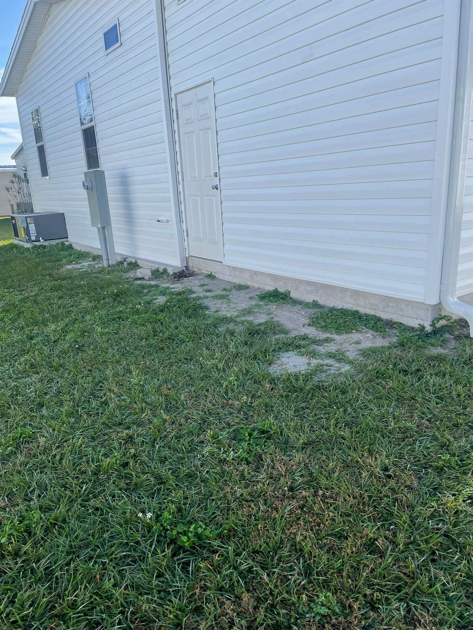 White building with a door, next to green grass and dirt.